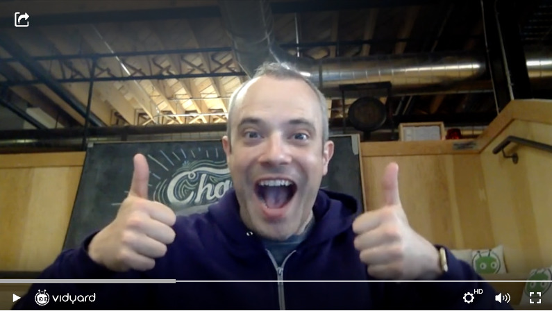 A screenshot of a Vidyard video featuring a male employee smiling at the camera and giving two thumbs up