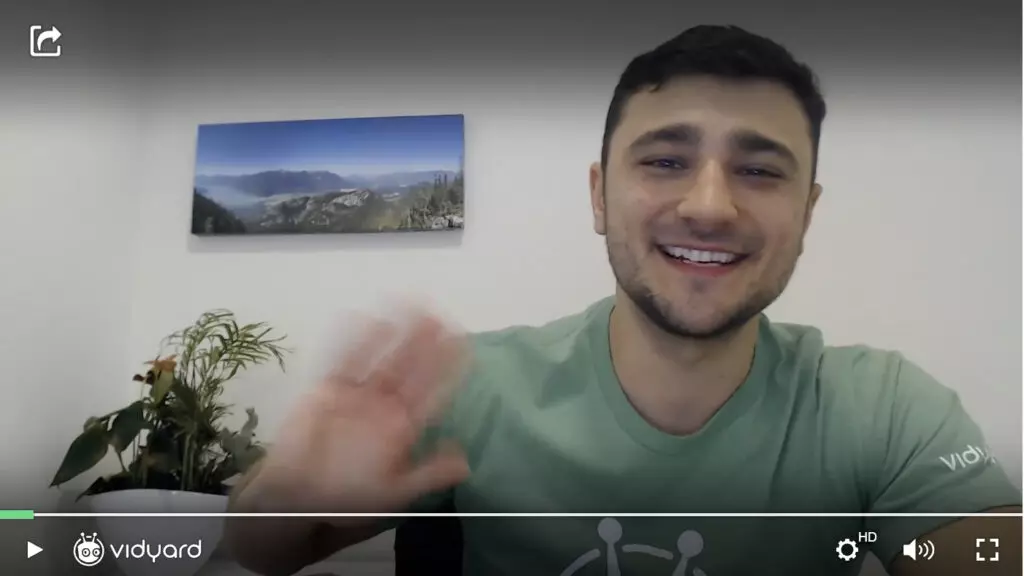 A sales professional in a green t-shirt smiling and waving at the camera.