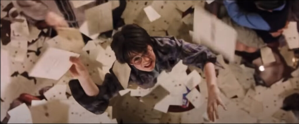 A screencap from Harry Potter and the Philosopher's Stone, showing Harry surrounded by a blizzard of Hogwarts letters.