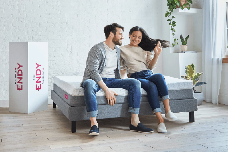 a man and woman sit on an Endy mattress