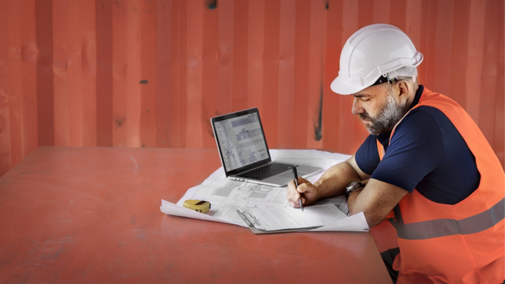 Photo of a man in a hard hat working on paperwork on a construction site