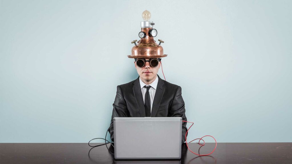Business man at a computer with an invention on his head to show he is using technology.