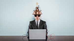 Business man at a computer with an invention on his head to show he is using technology.