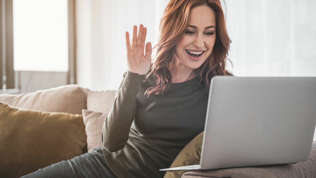 woman waves at her computer to make her video messaging personal