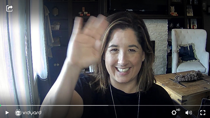 A screenshot of a Vidyard video featuring a female salesperson smiling and waving at the camera
