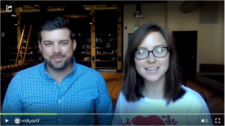 A screenshot of a Vidyard video featuring two people, a male salesperson and female salesperson each smiling at the camera