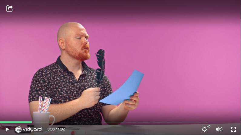 A screenshot of a Vidyard video featuring a male salesperson holding a piece of paper and a pen to his face as he thinks about what he will write.