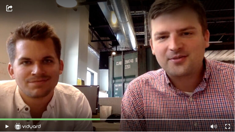 A screenshot of a Vidyard selfie video featuring two male salespeople smiling at the camera